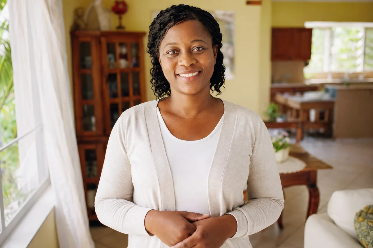A confident, professionally-dressed Jamaican caregiver at home